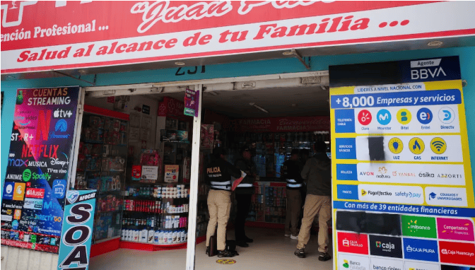 Calle Loreto en Piura con comercio de farmacia y publicidad de servicios financieros, streaming y plataformas de streaming, en un entorno urbano y comercial, con personas en la entrada de la tienda.