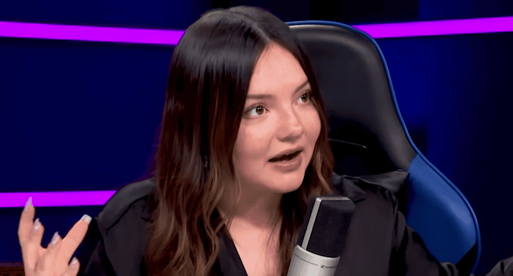 Comunicadora en entrevista en Loreto Noticias, haciendo una expresión facial de entusiasmo y gesticulando, en un estudio de televisión con fondo en tonos oscuros y luces moradas.