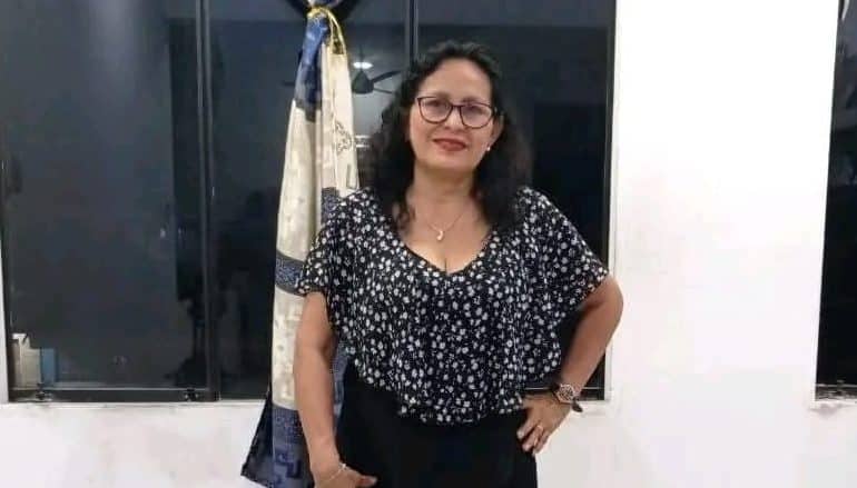 Profesional mujer en ambiente de oficina, vestida con blusa de estampado floral y gafas, posando con confianza en Loreto Noticias.