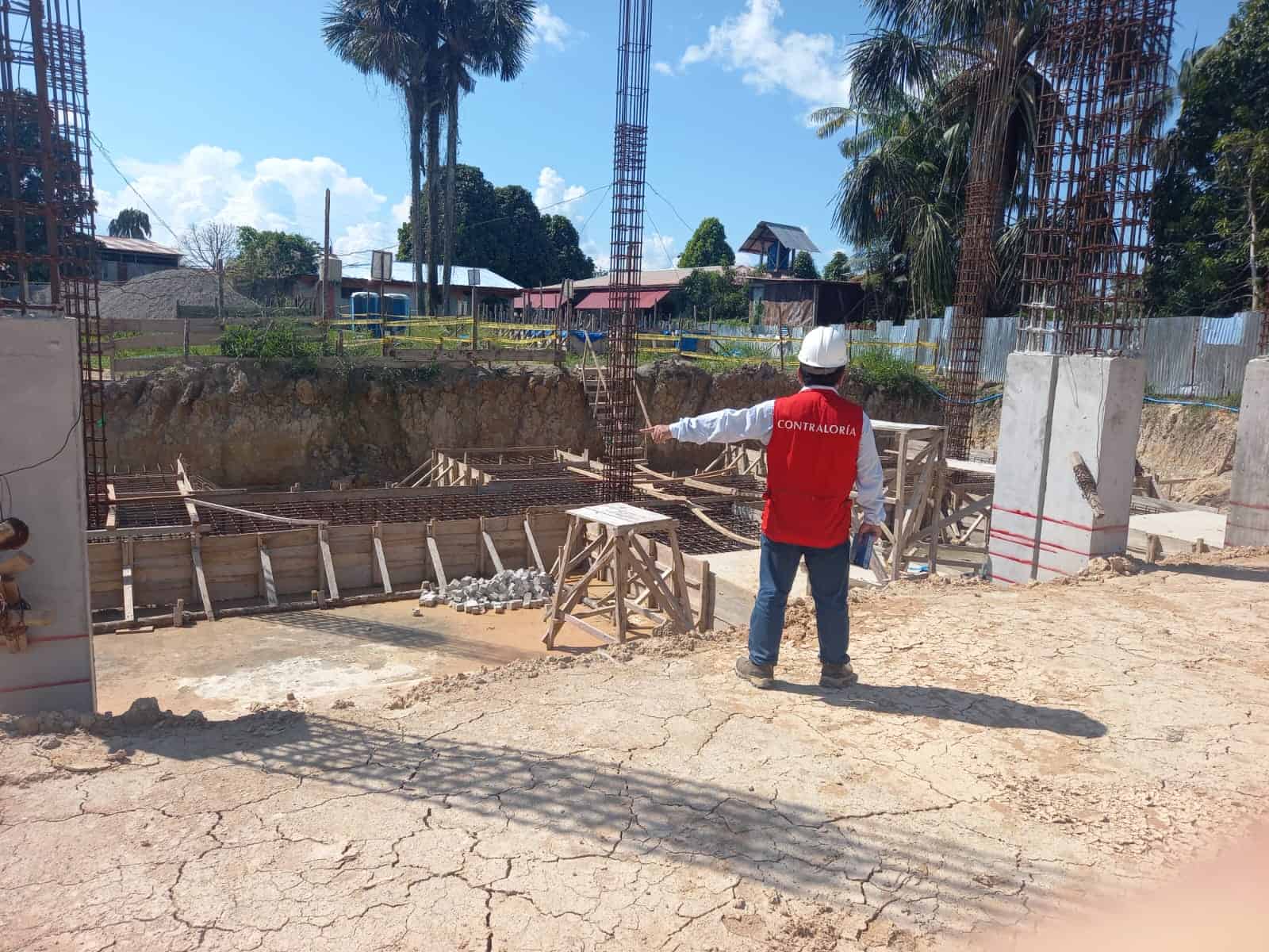 Contraloría supervisando obra en construcción en Loreto, Perú, con estructura de fierro y hormigón en proceso de edificación, en un entorno rural con casas y vegetación cercana.