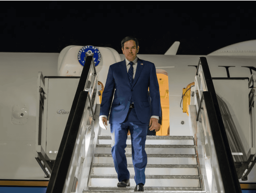 Mano en traje azul descendiendo por las escaleras del avión, en un contexto de viaje o llegada de un personaje importante, en la noche.