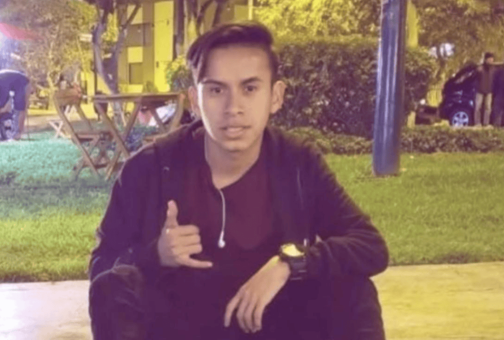 Joven en parque de Loreto haciendo señal de paz y mostrando confianza, ambiente al aire libre, gráficos de naturaleza y personas en fondo, imagen con significado de juventud y tranquilidad.