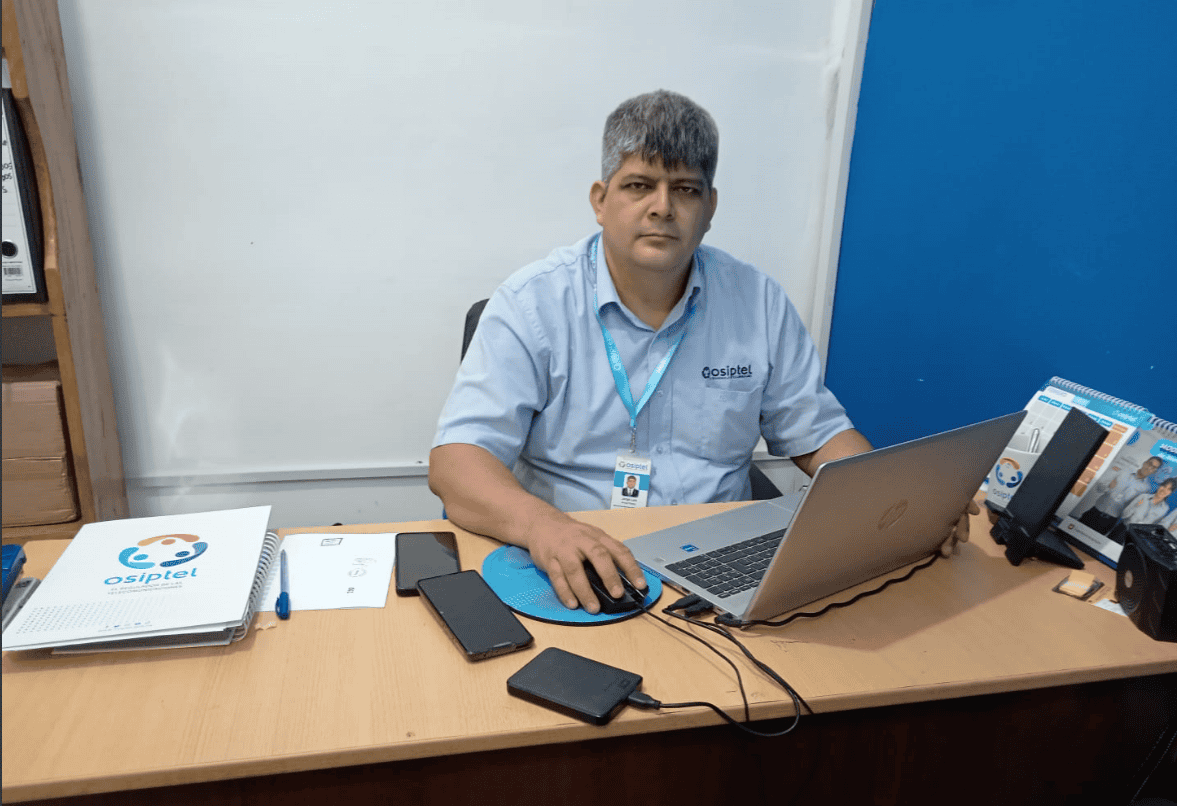 Asistente de atención en oficina con computadora portátil y teléfonos inteligentes, promocionando área de servicios tecnológicos en Loreto Noticias.