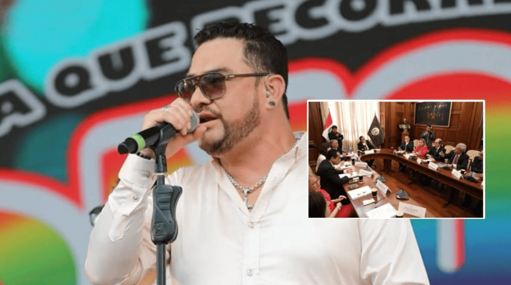 Alt: Hombre con gafas y barba hablando en un micrófono en un evento público con fondo colorido.