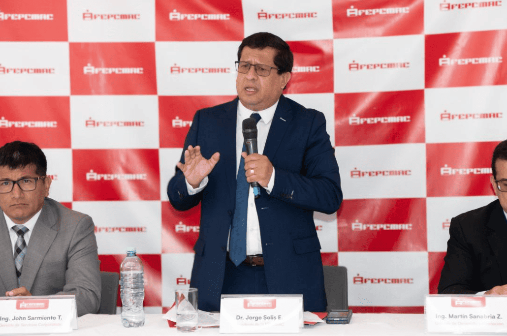 Llanto de Dr. Jorge Solis E en evento de Loreto Noticias, en centro de conferencias con logo de APRECAN en fondo rojo.