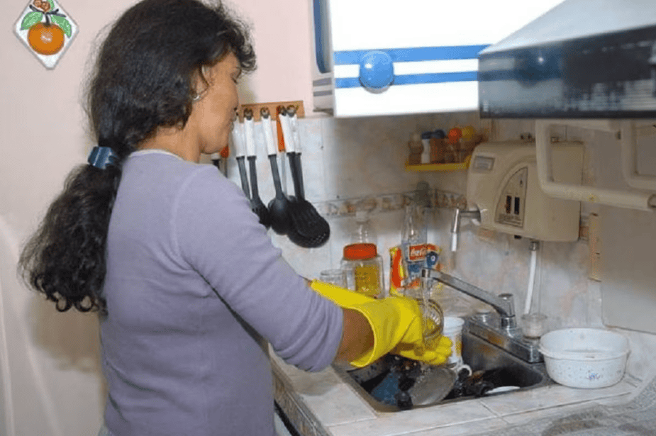 Lavadora de platos manejada por mujer con guantes amarillos en cocina peruana limpieza y organización.
