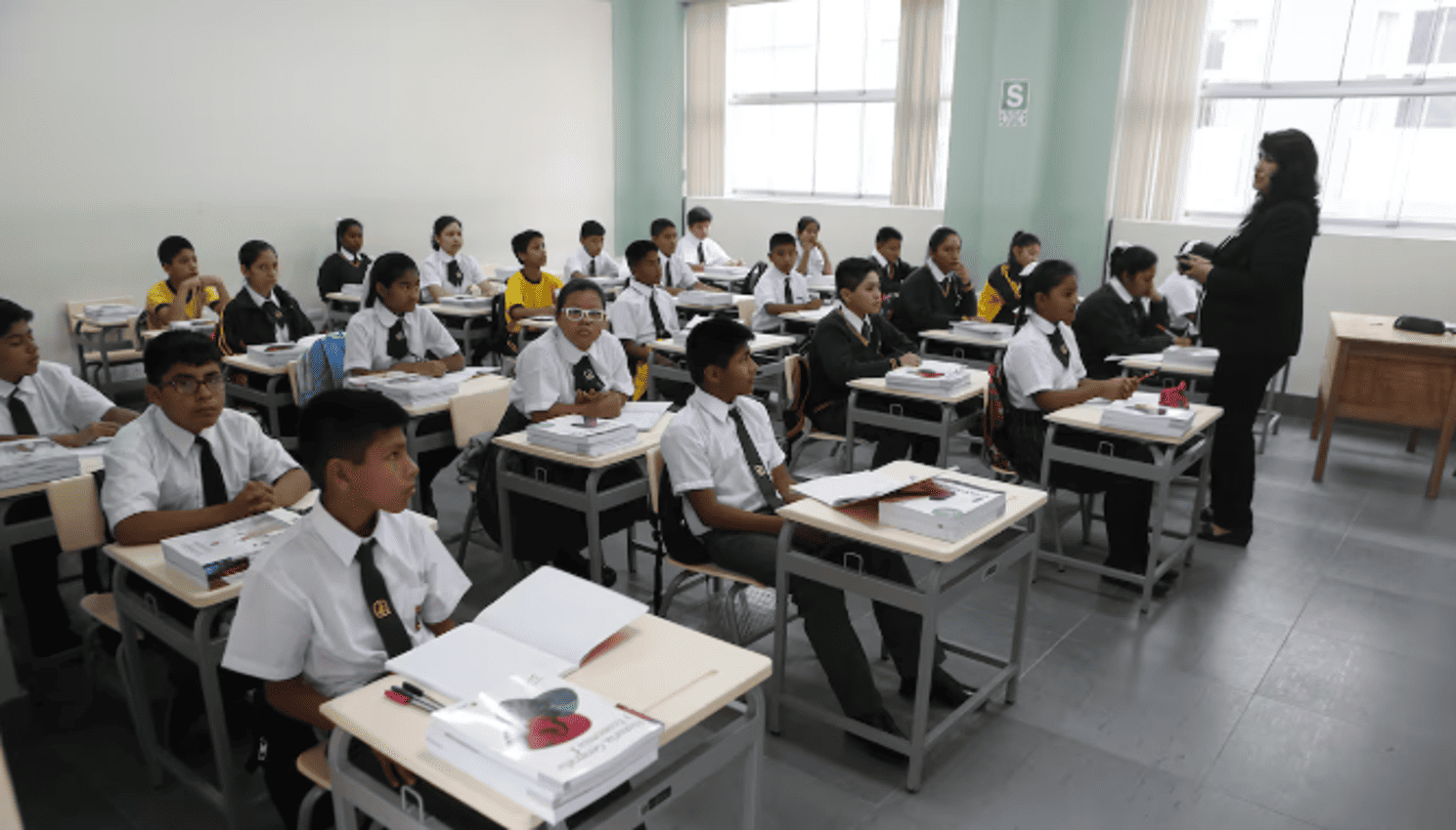 Estudiantes en aula de colegio de Loreto participando en clase con maestra en educación formal.