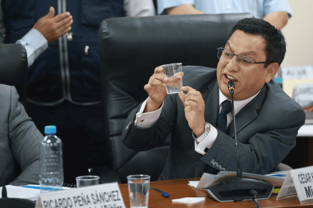 Barista en una reunión formal en oficina, tomando agua y usando gafas, con otros presentes en segundo plano, en un ambiente de trabajo empresarial y debates oficiales en Loreto Noticias.