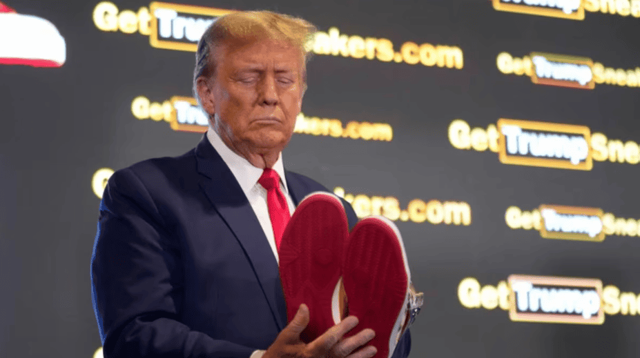 Trump con zapatos de colores rojos, en un evento con fondo de anuncios de la página GetTrumpSnacks.com, en la imagen de Loreto Noticias.