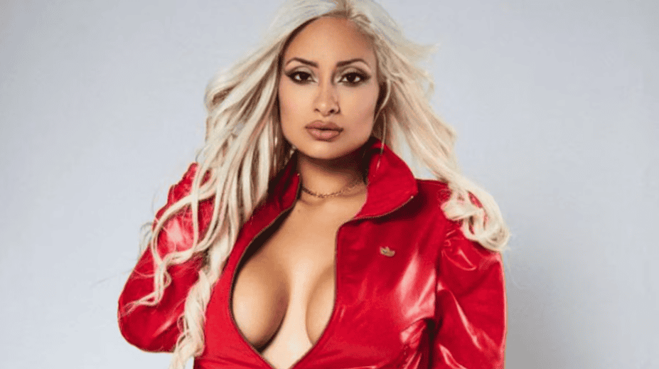 Chica con cabello rubio y peinado suelto, vestida con chaqueta roja y blusa ajustada, posando con expresión segura y mirada directa en fondo gris claro.