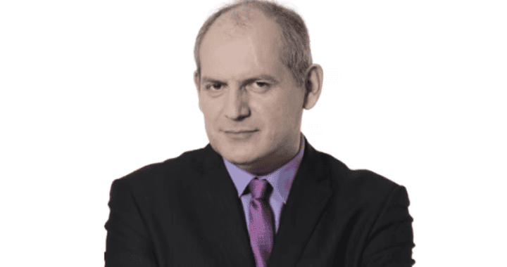 Hombre con traje serio, ajustando su chaqueta y mirando hacia la cámara, en un fondo blanco.