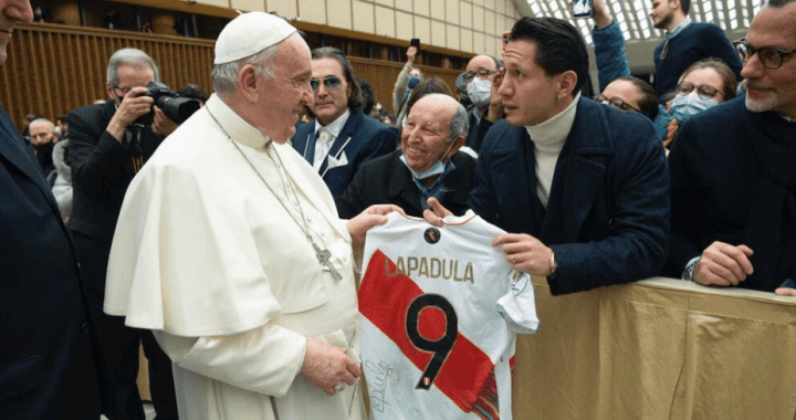 Jugador de fútbol peruano entregando camiseta a papa francisco en evento deportivo, público y prensa en fondo, en ceremonia internacional de la Liga Deportiva de la Papal, en Loreto Noticias.