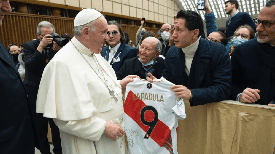 Jugador de fútbol peruano entregando camiseta a papa francisco en evento deportivo, público y prensa en fondo, en ceremonia internacional de la Liga Deportiva de la Papal, en Loreto Noticias.