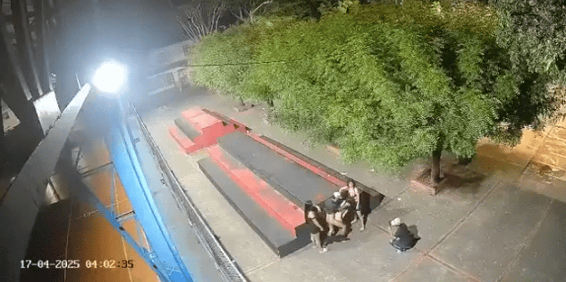 Personas conversando en una banca en la calle al anochecer, con árboles y farolas iluminando la acera en Loreto, Perú.