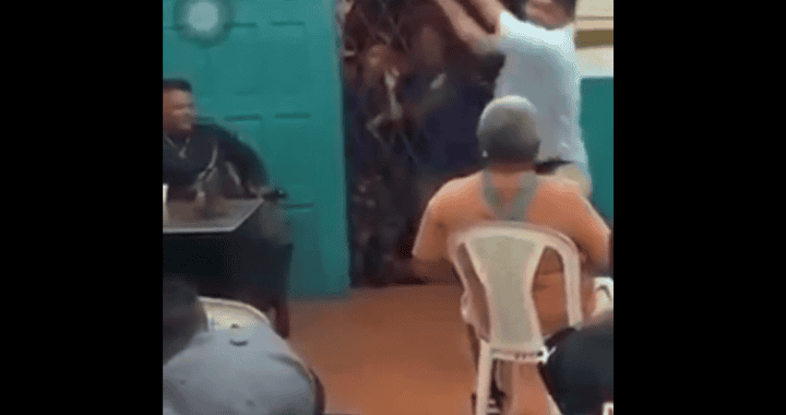 Cabra atacando a hombre en un evento público en Loreto, Perú, mientras otros asistentes observan y graben la escena con sus teléfonos. Hecho inusual en un ambiente social, causa asombro entre los presentes.