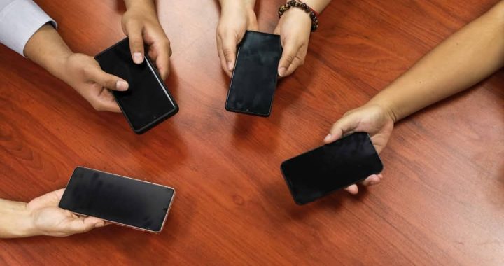 - Teléfonos inteligentes siendo sujetados por diferentes personas en una mesa de madera.