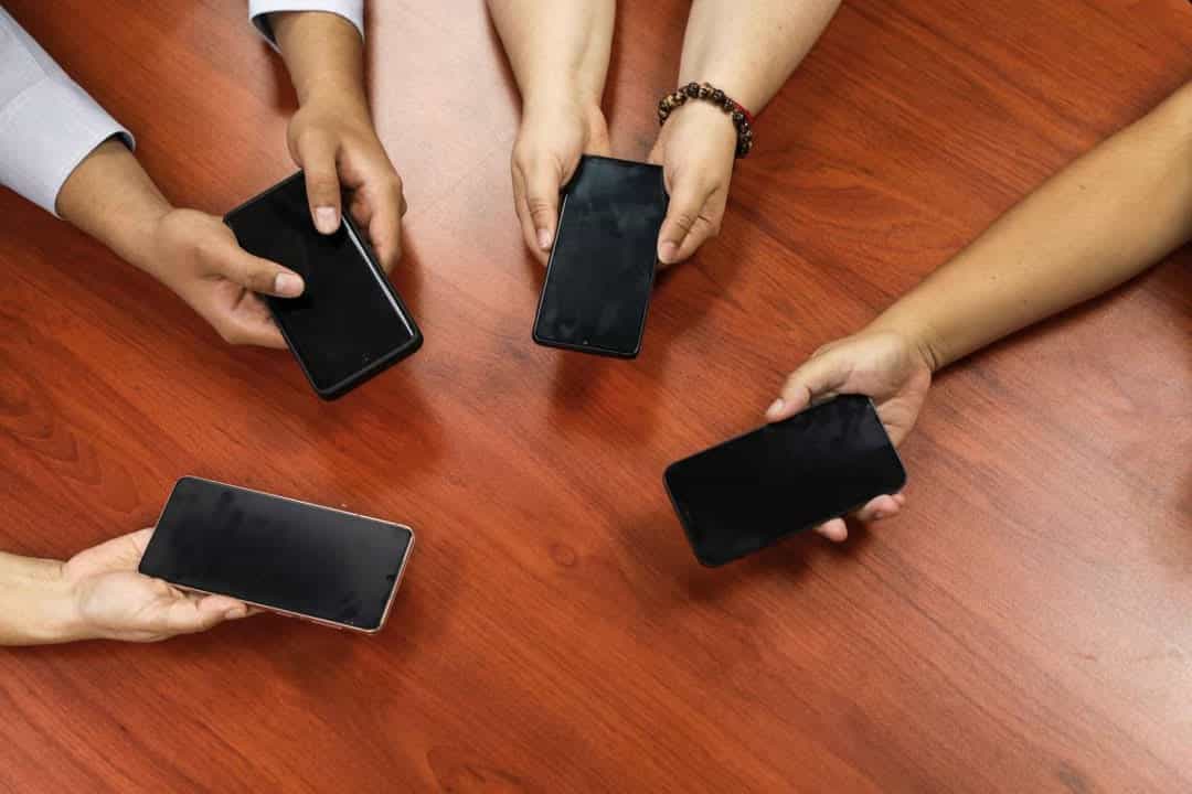- Teléfonos inteligentes siendo sujetados por diferentes personas en una mesa de madera.