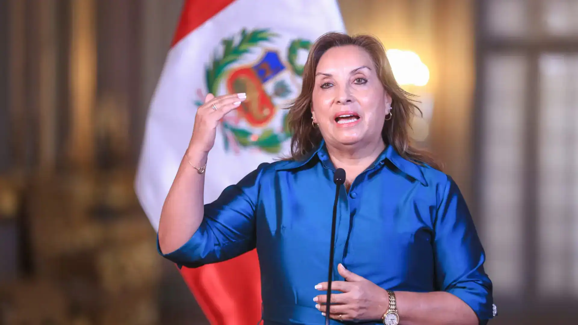 Peru, presidenta Dina Boluarte, dando un discurso durante una conferencia de prensa con la bandera peruana al fondo, destacando temas políticos y sociales en Loreto Noticias.