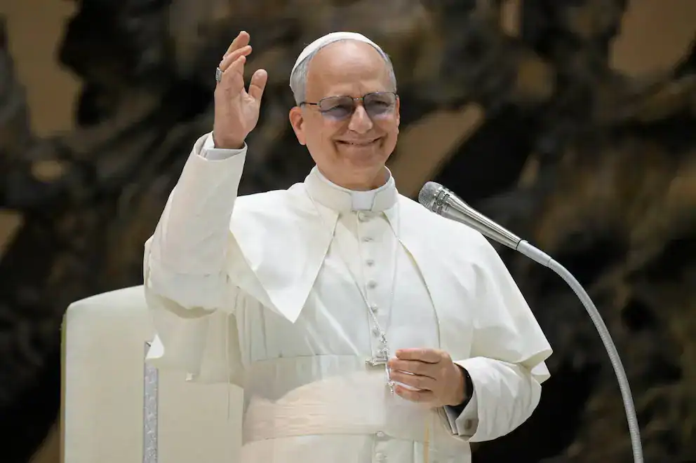 Papa Francisco en audiencia papal saludando con una sonrisa, vistiendo su vestimenta papal blanca y lentes de sol, en un evento oficial en el Vaticano.