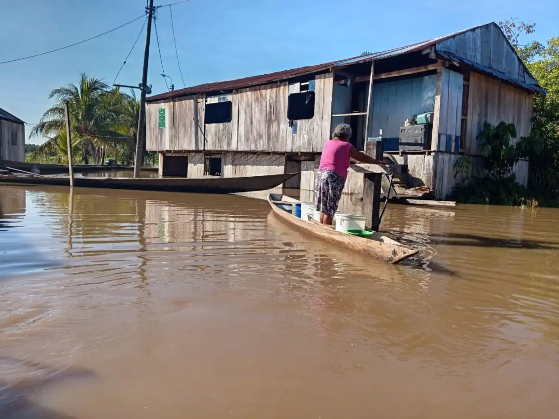 Barco y vivienda en una zona inundada en Loreto, Perú, mostrando el impacto de las lluvias intensas en comunidades ribereñas, con una mujer repartiendo suministros desde una canoa.