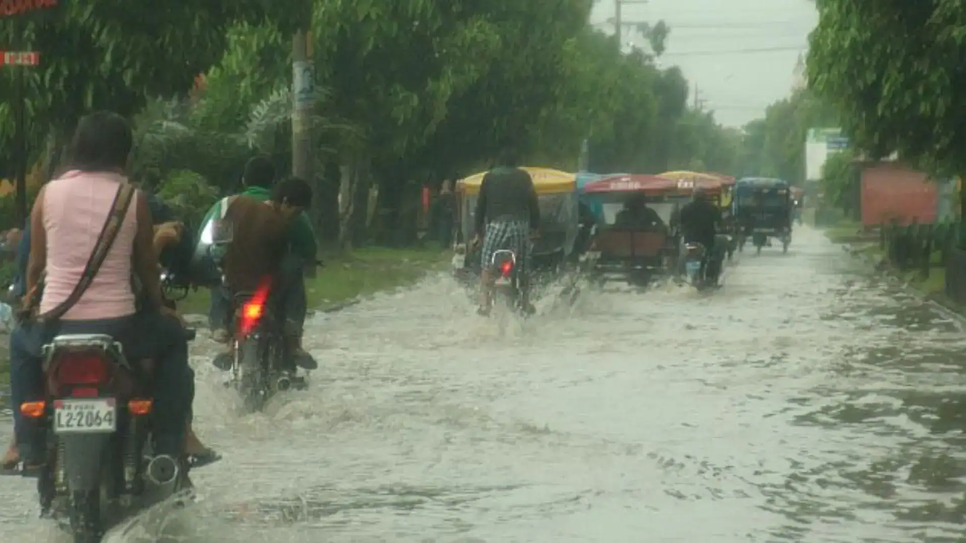 Lentes de lluvia en Loreto, Perú, durante lluvias intensas que afectan las calles y movilización de motos y carros. Comunidad enfrentando evento climático con precaución y adaptabilidad.