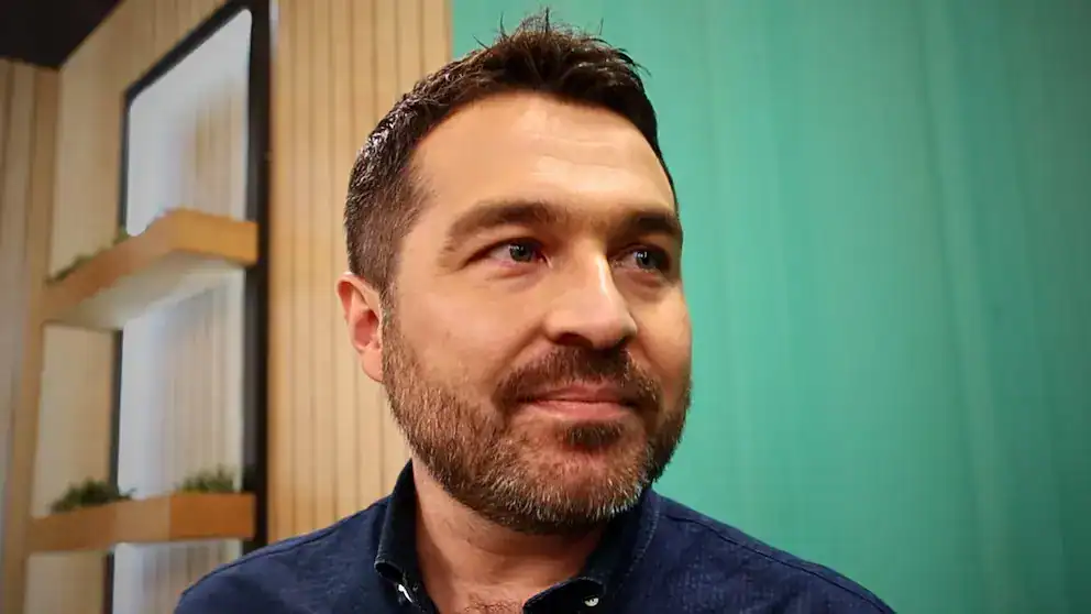 Hombre sonriendo en ambiente moderno, tecnología y coworking, imagen para noticias locales, digitalización y desarrollo empresarial.