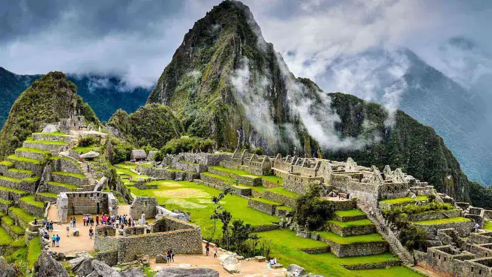 Majestuosas ruinas de Machu Picchu en Perú, patrimonio mundial, rodeadas de montañas verdes y nubes, representativas del turismo y cultura peruana.