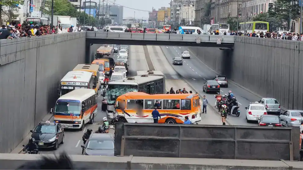 Accidente de tránsito en el túnel de Lima con congestión vehicular, pasajeros evacuando buses y motociclistas en la zona. Reporte de noticias locales sobre el impacto del accidente en la ciudad.