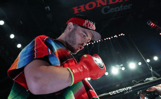 Luchador de boxeo con guantes rojos, en vestimenta tradicional y enfoque en preparación para la pelea en el ring, en un evento de boxeo profesional.