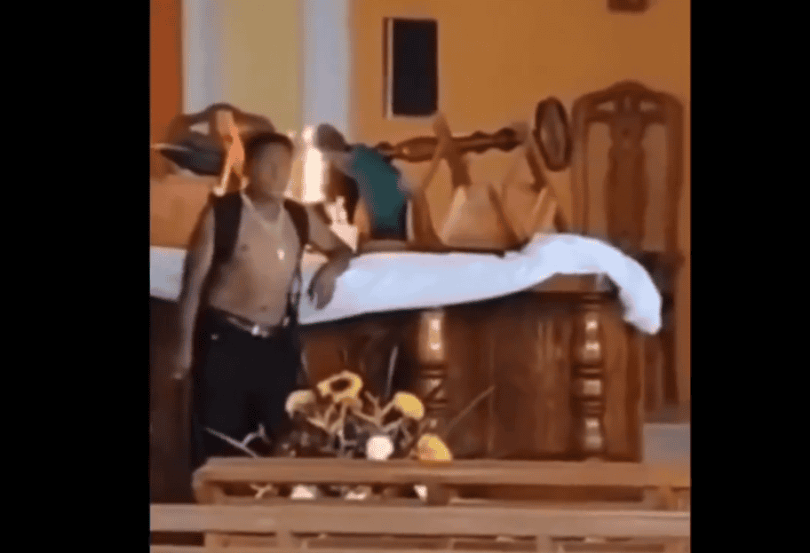 Sujeto en habitación con muebles de madera y decoración clásica, figura con mochila y pantalones cortos, ambiente interior, posible escena de sorpresa o accidente en un hotel o residencia en Loreto.