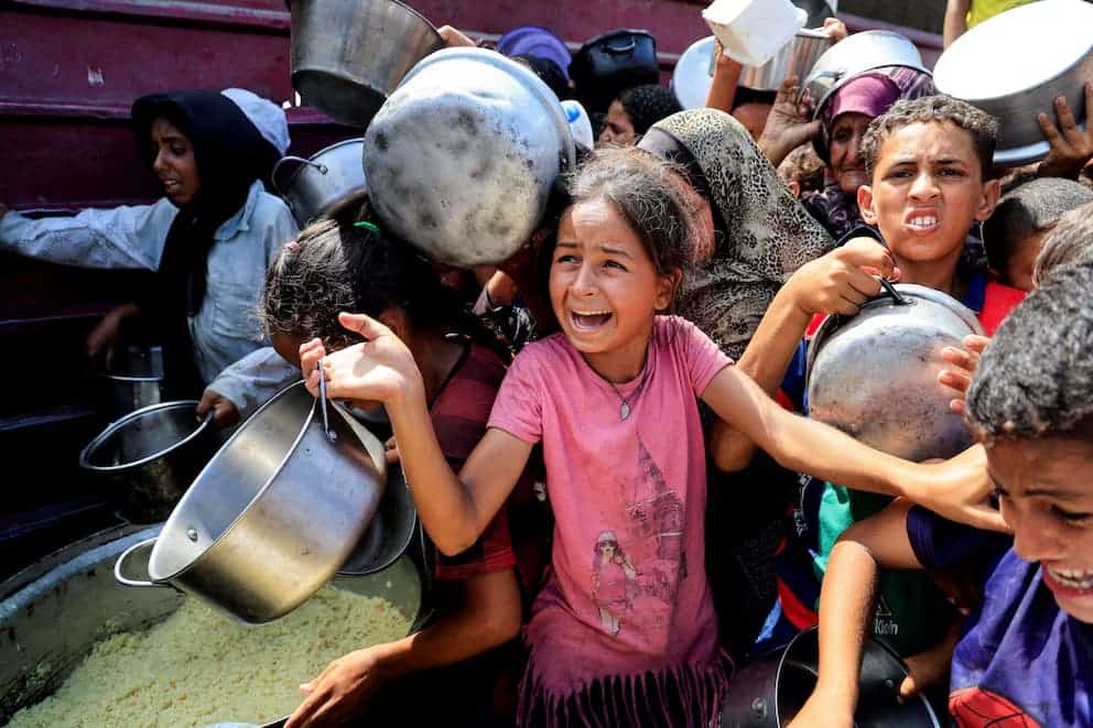 Lotes de niños y niñas en fila, llenando ollas con comida durante la distribución de ayuda humanitaria en Loreto, Perú. La escena refleja la solidaridad y las necesidades básicas en comunidades vulnerables de la Amazonía peruana.