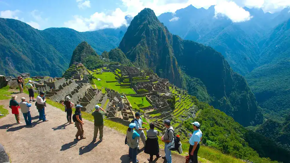 Machu Picchu, maravilla del Perú, con turistas fascinados explorando la histórica ciudadela inca en medio de las impresionantes montañas verdes.