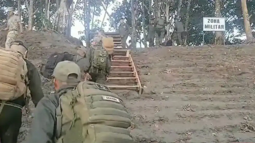 Zarpe militar en área forestal de Loreto, Perú, con soldados en marcha escalando una pendiente y señalización de zona militar en fondo.