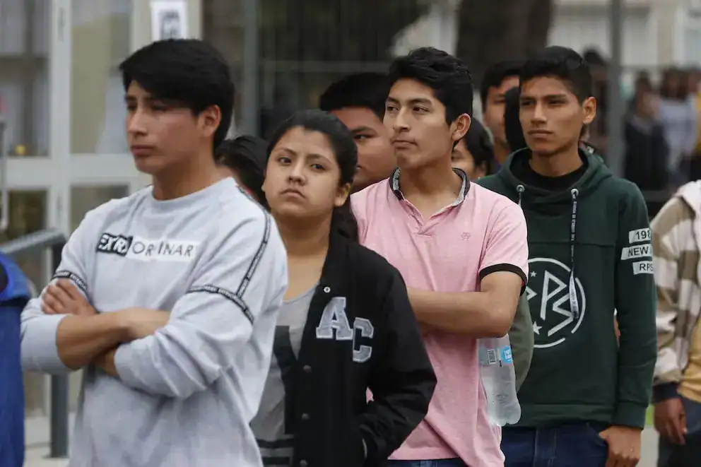Jóvenes en fila, esperando en una fila, en un entorno urbano, con expresión de incertidumbre, en un contexto social y cultural en Loreto, Perú, resaltando temas de juventud, comunidad y cotidianeidad.