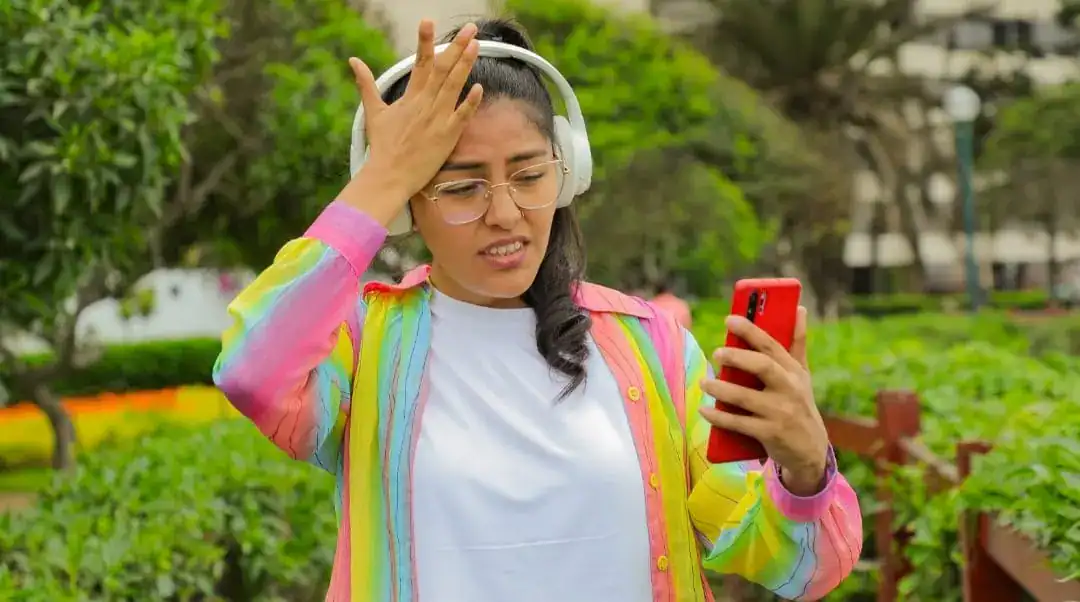 Nina con auriculares y teléfono móvil en un parque, mostrando incomodidad o frustración, en un entorno natural, resaltando temas de salud mental, estrés y tecnología en las noticias de Loreto Noticias.