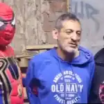 Disfraz de Spider-Man, estilo del superhéroe, vistiendo una camiseta azul con el logo de Old Navy, y acompañados por otros hombres, en un ambiente informal.