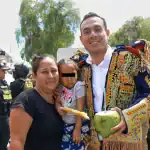 Bebé acompañada por una mujer y un hombre con traje tradicional, Policía y autoridades en evento cultural y social en Loreto, Perú.