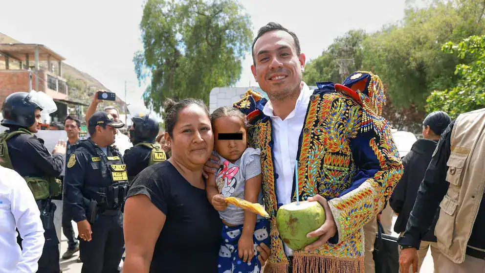 Bebé acompañada por una mujer y un hombre con traje tradicional, Policía y autoridades en evento cultural y social en Loreto, Perú.