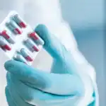 Una mano con guantes sostiene un blister con cápsulas de medicamentos rojos y blancos, símbolo de avances en salud y medicina en Loreto, Perú.