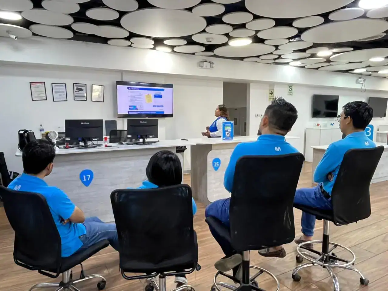 - Personas atendiendo en oficina de Loreto Noticias, con empleados en uniforme azul y tecnología moderna.