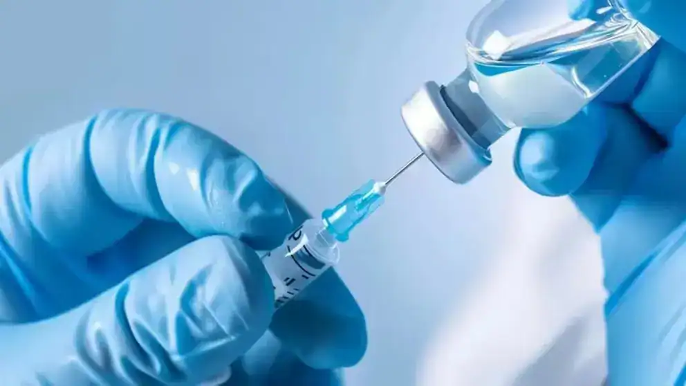 Imagen de un profesional de la salud preparando una vacuna contra el COVID-19 con un jeringa y una ampolla, demostrando avances en inmunización y salud pública.